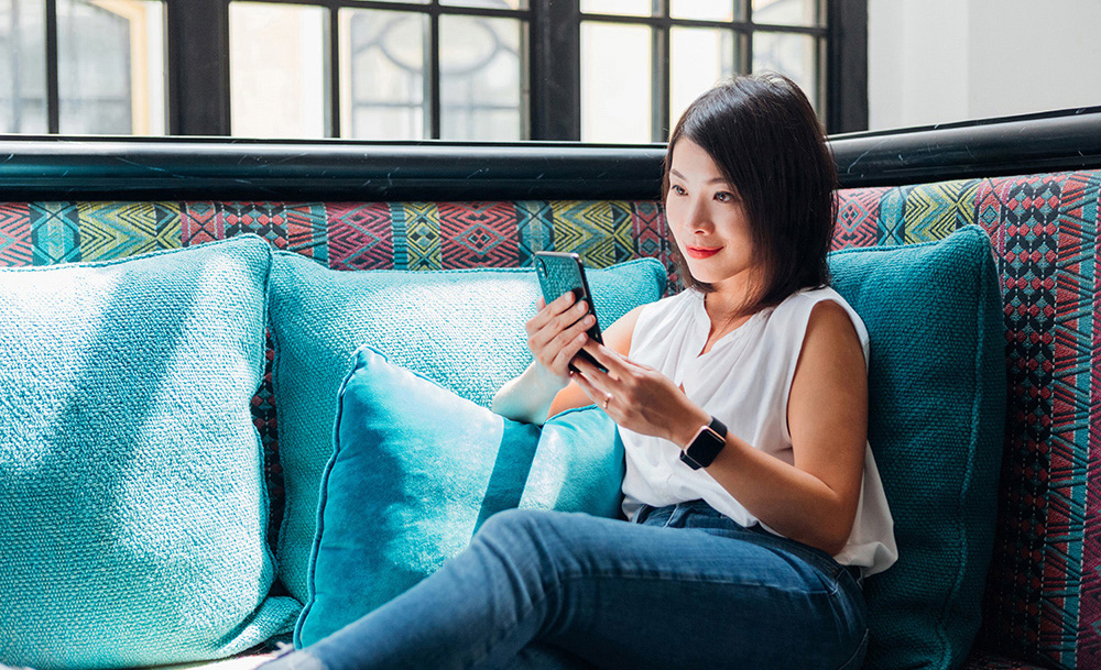 A young woman looks at her cell phone amidst blue pillows.